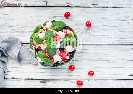 Italian pasta salad with fresh tomatoes, black olives, red onion mozzarella cheese balls, basil, and an olive oil dressing. Image shot from above. Stock Photo