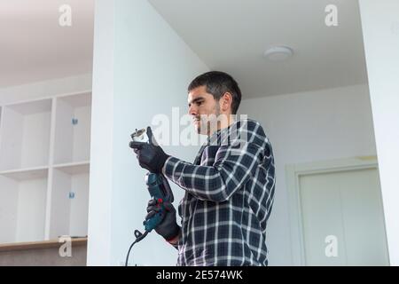 A carpenter with a circular drill drilling holes in the kitchen shelves before placing them in a predetermined place on the wall. Stock Photo