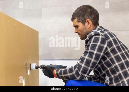 A carpenter with a circular drill drilling holes in the kitchen shelves before placing them in a predetermined place on the wall. Stock Photo