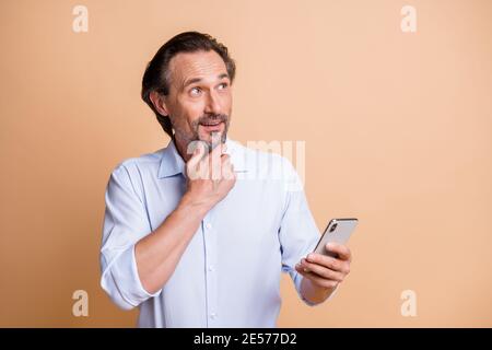 Portrait of nice cheerful middle aged man thinking using device copy space isolated over beige pastel color background Stock Photo