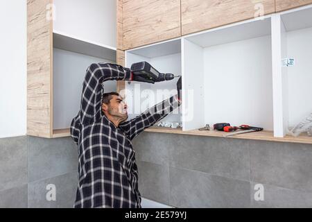 The carpenter finalizing the assembly of the kitchen shelf on the wall. Stock Photo