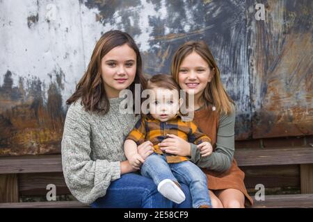 Two sisters and a little baby brother sitting on steps outside for a portrait Stock Photo