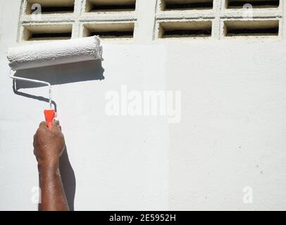 Painter painting white acrylic on house concrete wall with a paint roller, The sunburned hand of the laborer Stock Photo