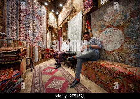 Istanbul / Turkey - May 02 2019 : Carpet shop and a salesperson with the owner are in the Grand bazaar, inside the shop decorated with large carpets h Stock Photo