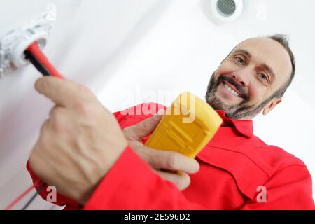 happy electrician checking voltage in electrical wall socket Stock Photo
