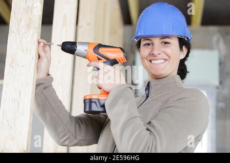 smiling young professional woman using cordless screwdriver on wood Stock Photo