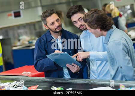 three male workers in discussion while looking at clipboard Stock Photo