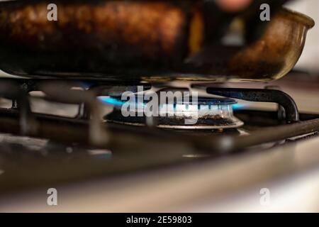 Close up of and old and dirty gas stove with a pan on top. Fire is on and something is cooking. Stock Photo