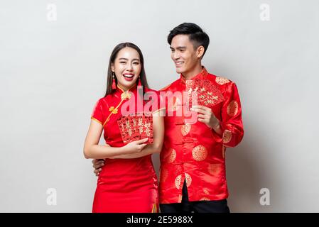 Happy Asian couple in traditional oriental costumes holding red envelopes or Ang Pao in light gray background for Chinese new year concepts,  texts me Stock Photo