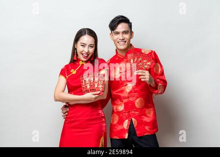 Happy Asian couple in traditional oriental costumes holding red envelopes or Ang Pao in light gray background for Chinese new year concepts,  texts me Stock Photo
