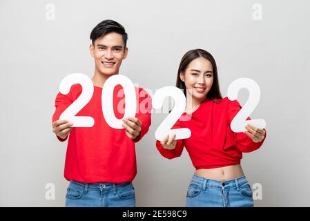 Happy Asian couple smiling and showing number 2022 for new year concept on light gray studio background