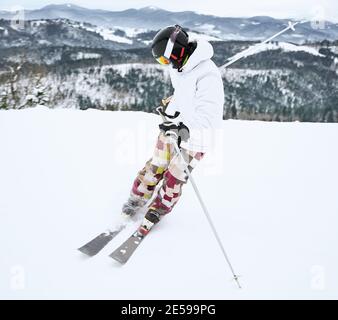 Image of skier in ski equipment, captured in motion doing trick in snowy mountains in full length. Beautiful landscape on background. Winter sports concept Stock Photo