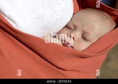Newborn boy sleeping in the orange baby sling carrier outdoor Stock Photo