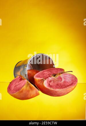 An apple with red pulp inside with a carved wedge on the background of a bucket. Yellow background isolated. Exotic fruits, healthy food Stock Photo