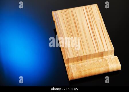 Wooden desktop mobile phone holder with hand-held phone isolated on blue black background. Creativity and technology concept Stock Photo