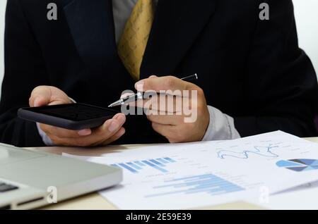 Business men hand holding cell phones and pens on the desk have business documents graphs financial reports Stock Photo