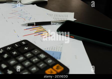 Mobile Phones business documents graphs and chart accounting finance, marketing and reports and pen on desk. Stock Photo