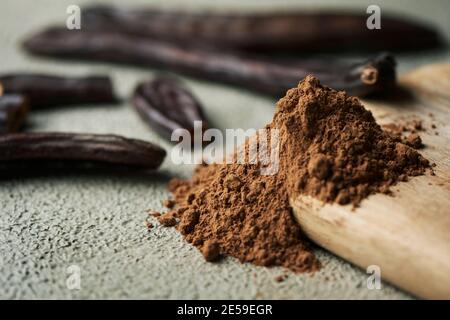 closeup of some ripe carob pods and a pile of carob powder on a textured gray surface Stock Photo