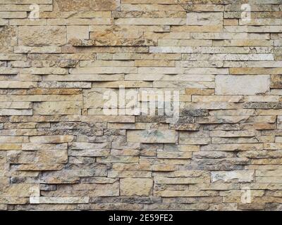 Wall with decorative beige embossed cladding of narrow granite tiles with gray spots Stock Photo