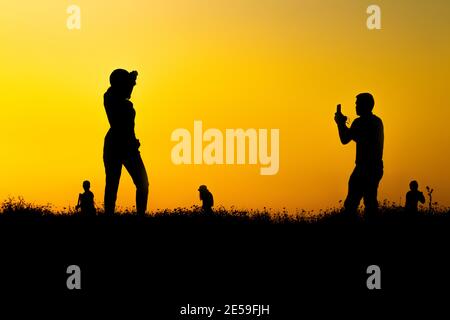 Silhouette of many tourists are taking pictures by smart phone on the top of the mountain during sunset times. Stock Photo
