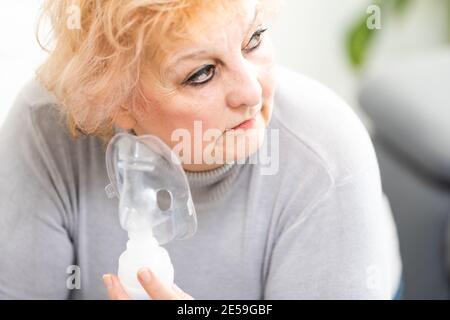 Elderly woman using asthma machine on light background Stock Photo