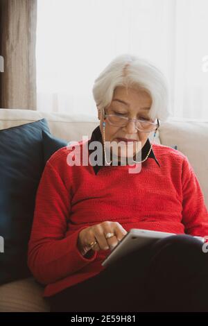 woman in red sweater sitting on white sofa, got bad news on phone Stock Photo