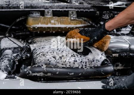 Close up of car wash worker wearing protective gloves and washing car engine with soapy sponge. Cleaning services. Stock Photo