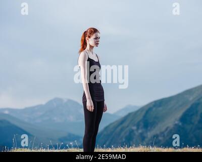 A slender woman is engaged in yoga in nature in the mountains in leggings and a T-shirt Stock Photo
