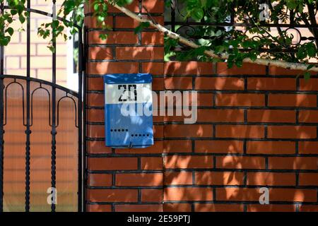 A blue mailbox hangs on the fence. Number 20. Red brick and birch are visible. Stock Photo