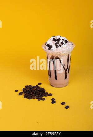 Milkshake with coffee topping. Iced chocolate with whipped cream on a yellow background. Coffee beans Stock Photo