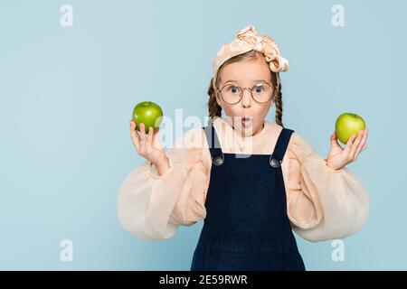 surprised kid in glasses holding green apples isolated on blue Stock Photo