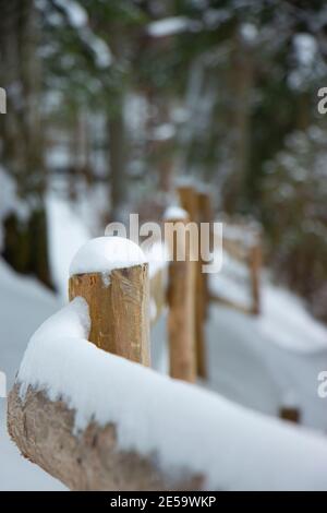 wooden pole handrail bent beige fence winter road in the forest. yellow bars snow cap Stock Photo