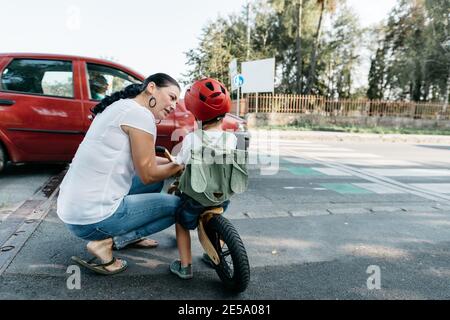 Mother and a child waiting at a zebra crossing with a car passing by. Rear view of a young boy on a bike listening to his mother explaining road saf