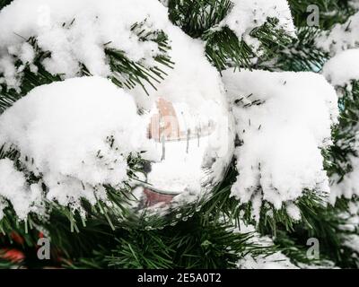 mirrored silver ball on outdoor decorated snow-covered Christmas tree close up on overcast winter day Stock Photo
