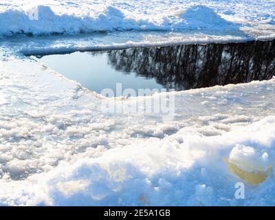 deep ice-hole in frozen snow-covered pond on cold sunny winted day Stock Photo
