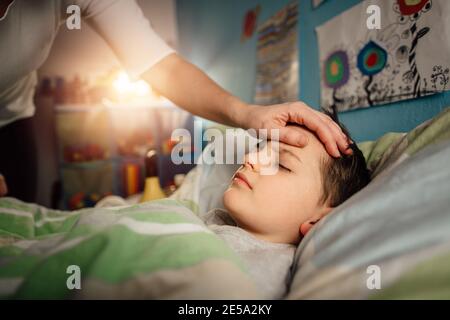 A sick child sweating and lying in a bed with a high temperature. A mother looking after her ill son at home in the night. Stock Photo