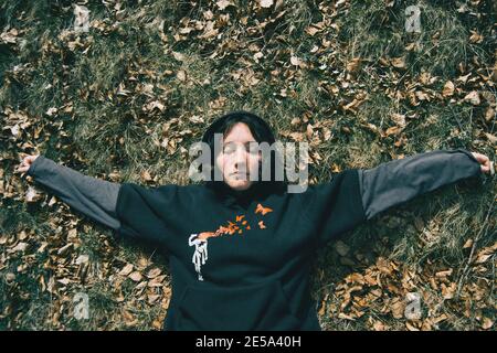 A girl with closed eyes and arms crossed resting on the ground in nature Stock Photo