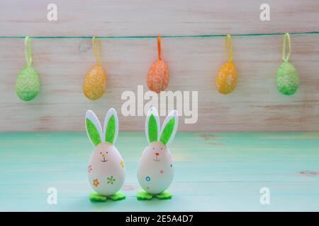 Easter rabbits toys, row of hanging eggs on vintage wood background. Funny Easter decoration with copy space. Easter mood. Stock Photo