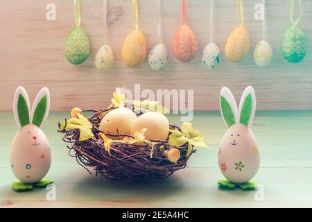 Easter rabbits toys, eggs in nest and row of hanging eggs on vintage wood background. Easter mood. Funny Easter decoration. Stock Photo