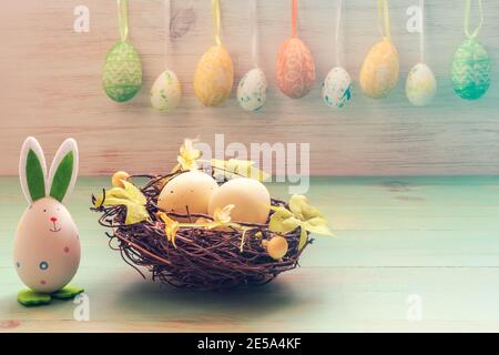 Easter rabbits toy, eggs in nest of twigs and row of hanging eggs in soft light on vintage wood background. Easter mood decoration. Funny Easter conce Stock Photo
