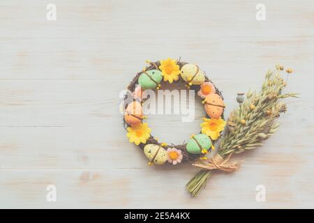 Wreath decorated with pastel colors Easter eggs and flowers, next to flower bouquet on vintage wooden background. Colorful Easter background. Spring w Stock Photo