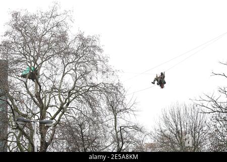HS2 Rebellion protester on a zip line between two trees in an encampment in Euston Square Gardens in central London, where the protesters have built a 100ft tunnel network, which they are ready to occupy, after claiming the garden is at risk from the HS2 line development. Picture date: Wednesday January 27, 2021. Stock Photo