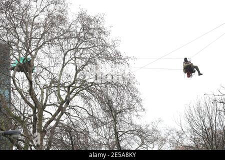 HS2 Rebellion protester on a zip line between two trees in an encampment in Euston Square Gardens in central London, where the protesters have built a 100ft tunnel network, which they are ready to occupy, after claiming the garden is at risk from the HS2 line development. Picture date: Wednesday January 27, 2021. Stock Photo