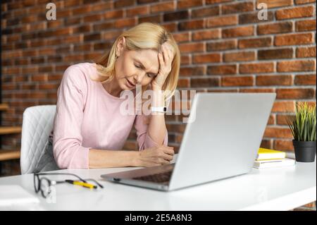 Fatigued middle-aged woman using laptop for working, a female employee in smart casual wear feels headache, tired and burnout, sitting at the desk in