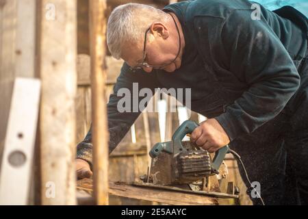 Carpenter cutting a piece of wood in his woodwork workshop, using a saw Stock Photo