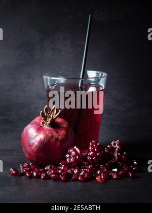 Pomegranate juice in a glass with cocktaile straw and fresh grenadine fruit on the table at black background. Popular fruit in Azerbaijan and Turkey. Stock Photo