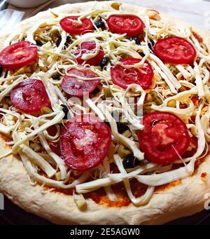 Pizza with tomato, mozzarella cheese, black olives and peppers. Ready to be cooked. Selective focus tomato Stock Photo