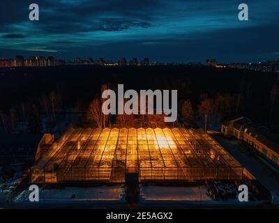 Glowing modern glass greenhouse in winter night, aerial view. Stock Photo