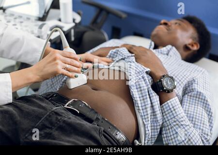 Close up cropped image of ultrasound diagnostics of abdomen of young African man by modern ultrasound equipment. Young man getting ultrasound from Stock Photo