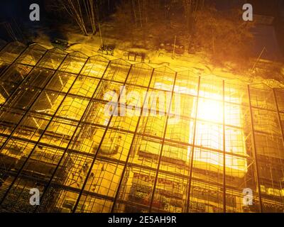 Glowing modern glass greenhouse in winter night, aerial view. Stock Photo